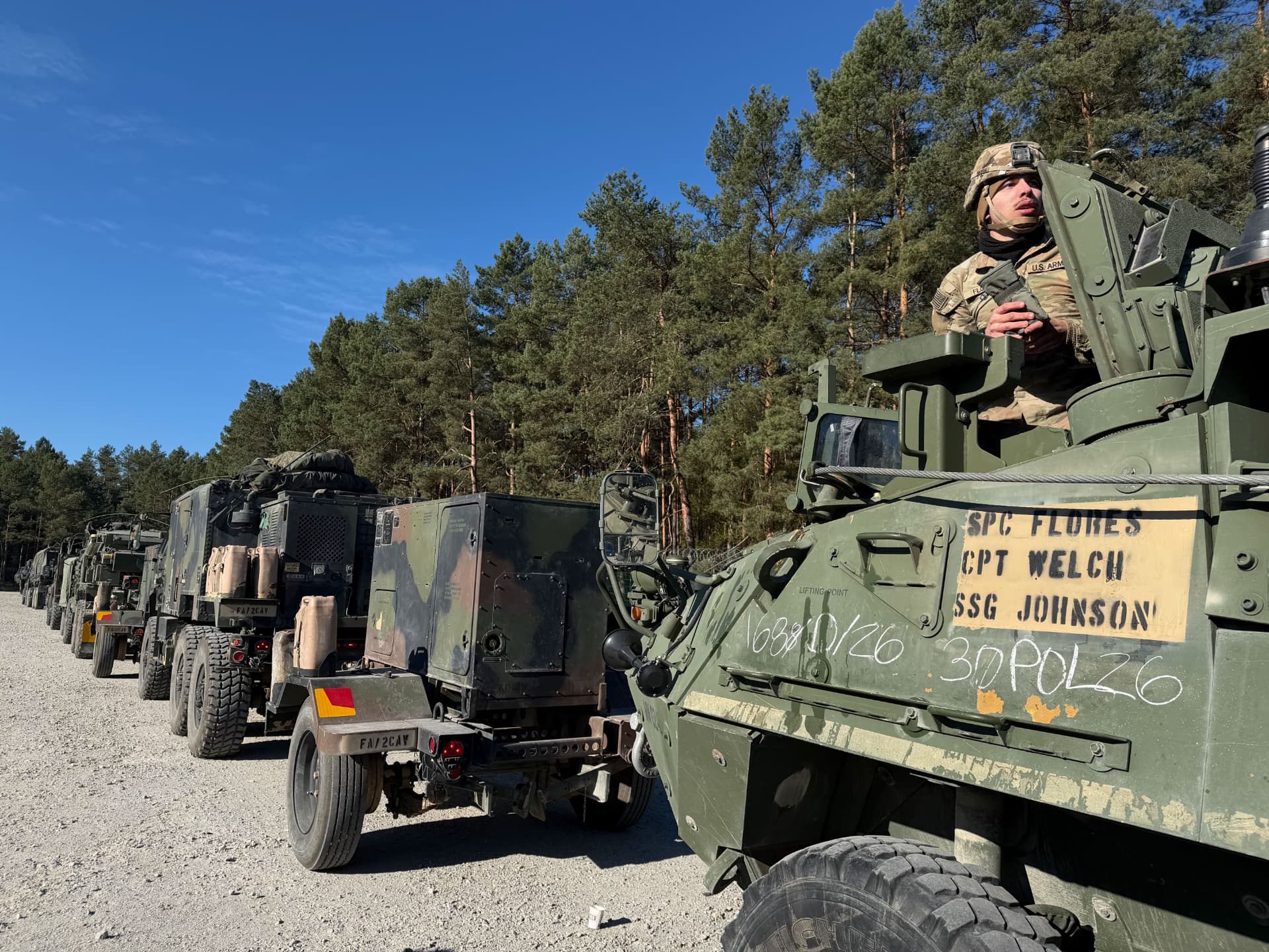 A convoy of armoured vehicles staged along a gravel road during a training rotation.