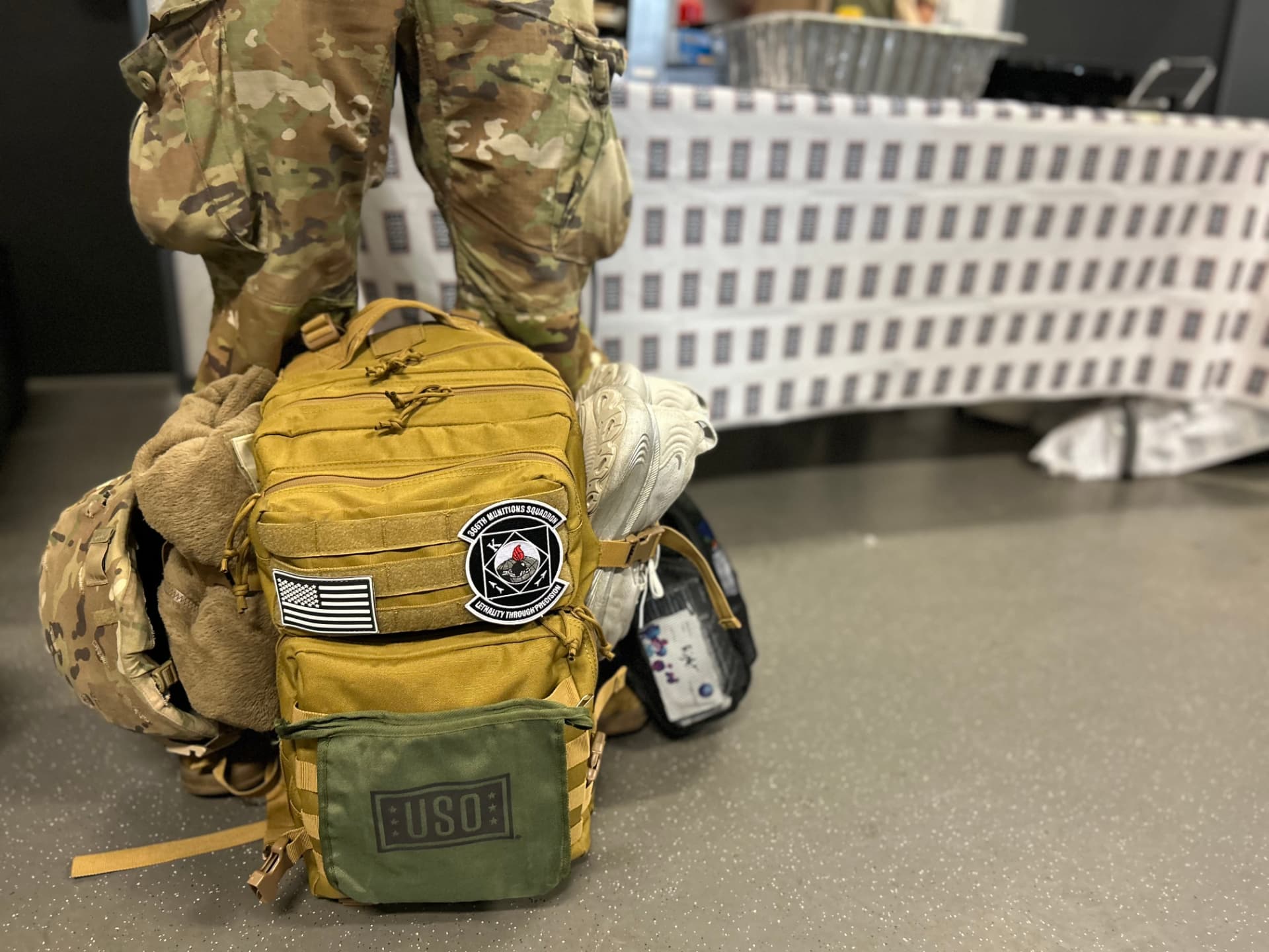 A USO care pack attached to a rucksack resting on the floor of a departure area.