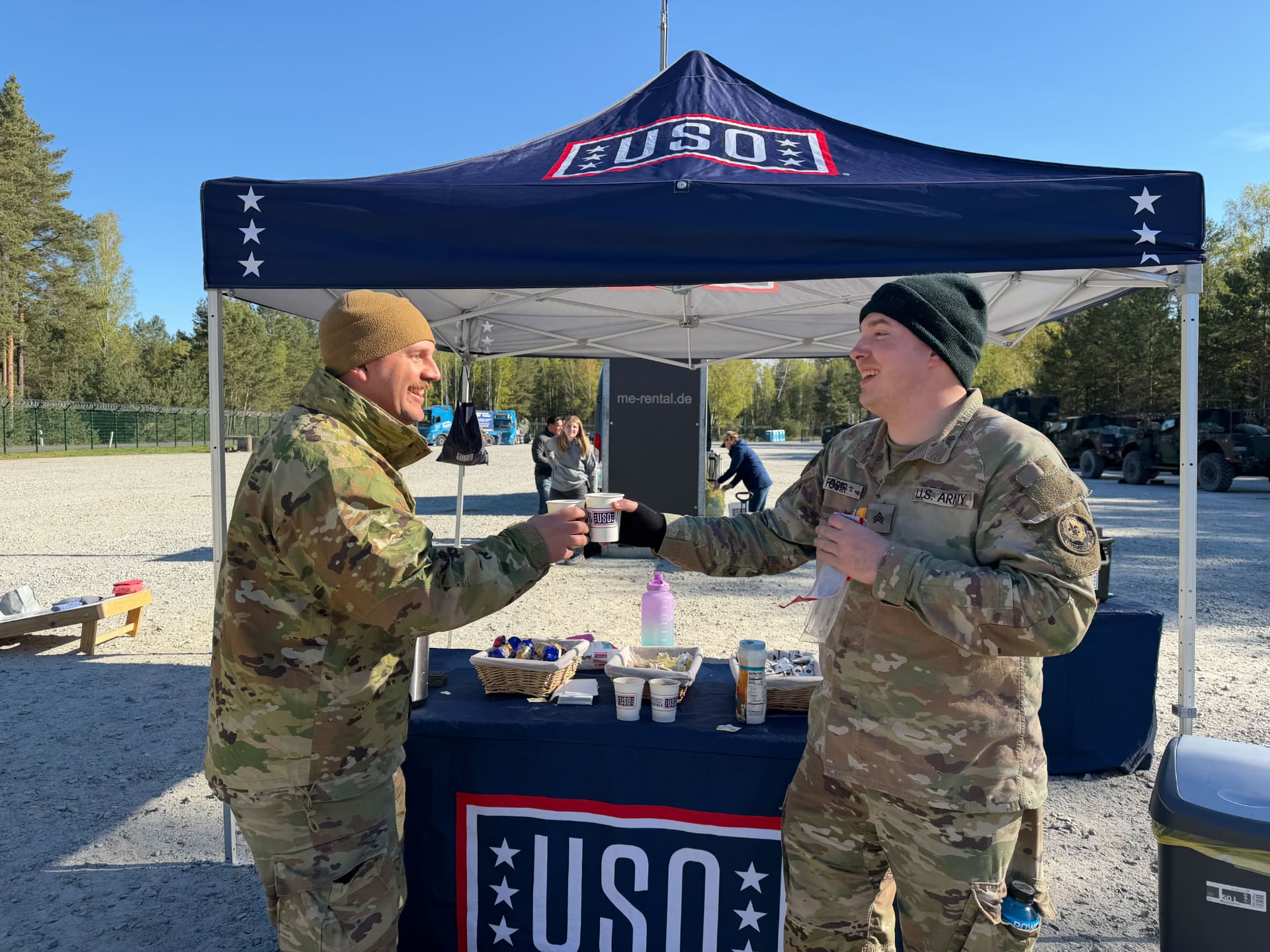 Two soldiers sharing coffee and laughing at a USO service point under a USO canopy.