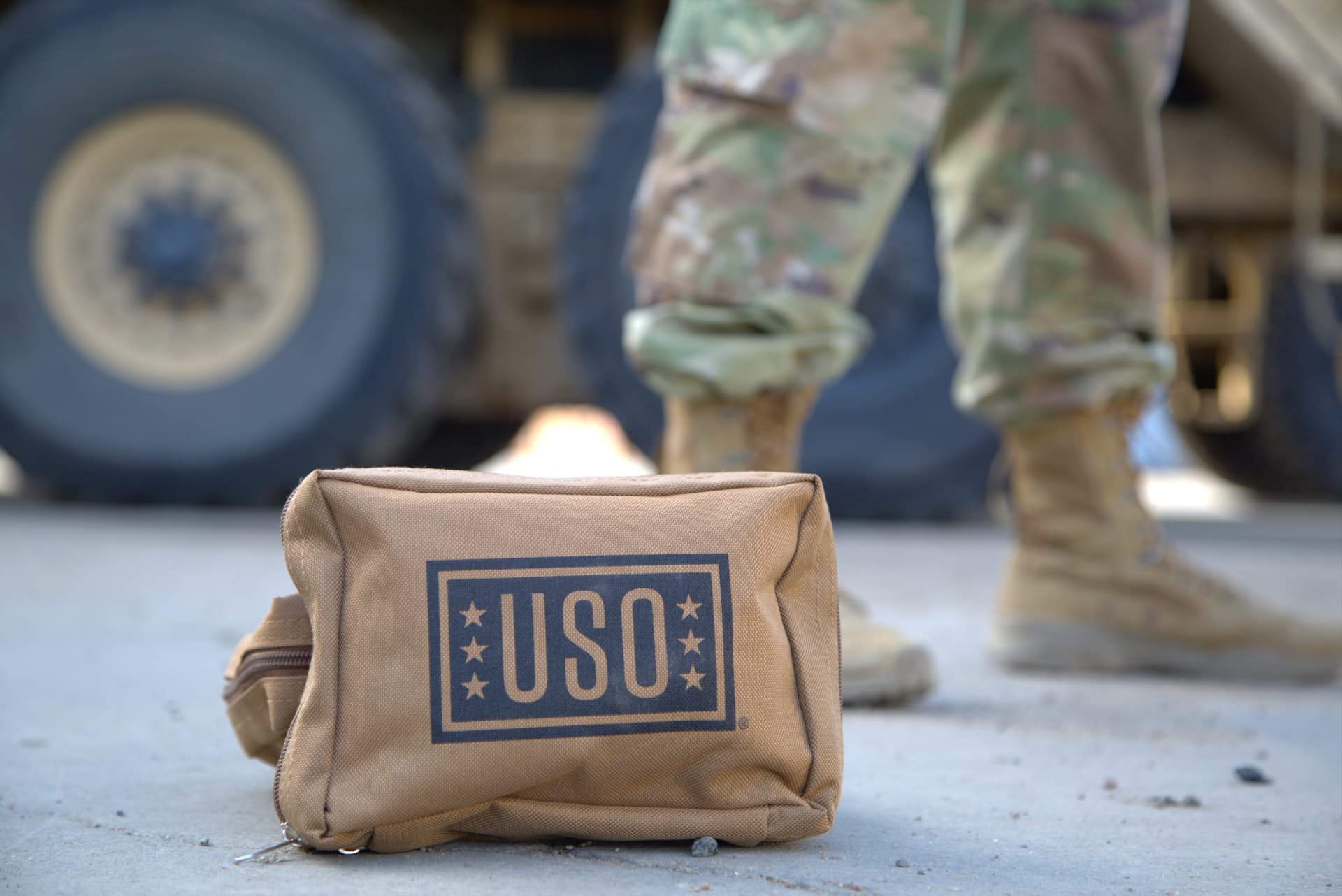 A USO care pack sitting on the ground in front of a soldier and a military vehicle.