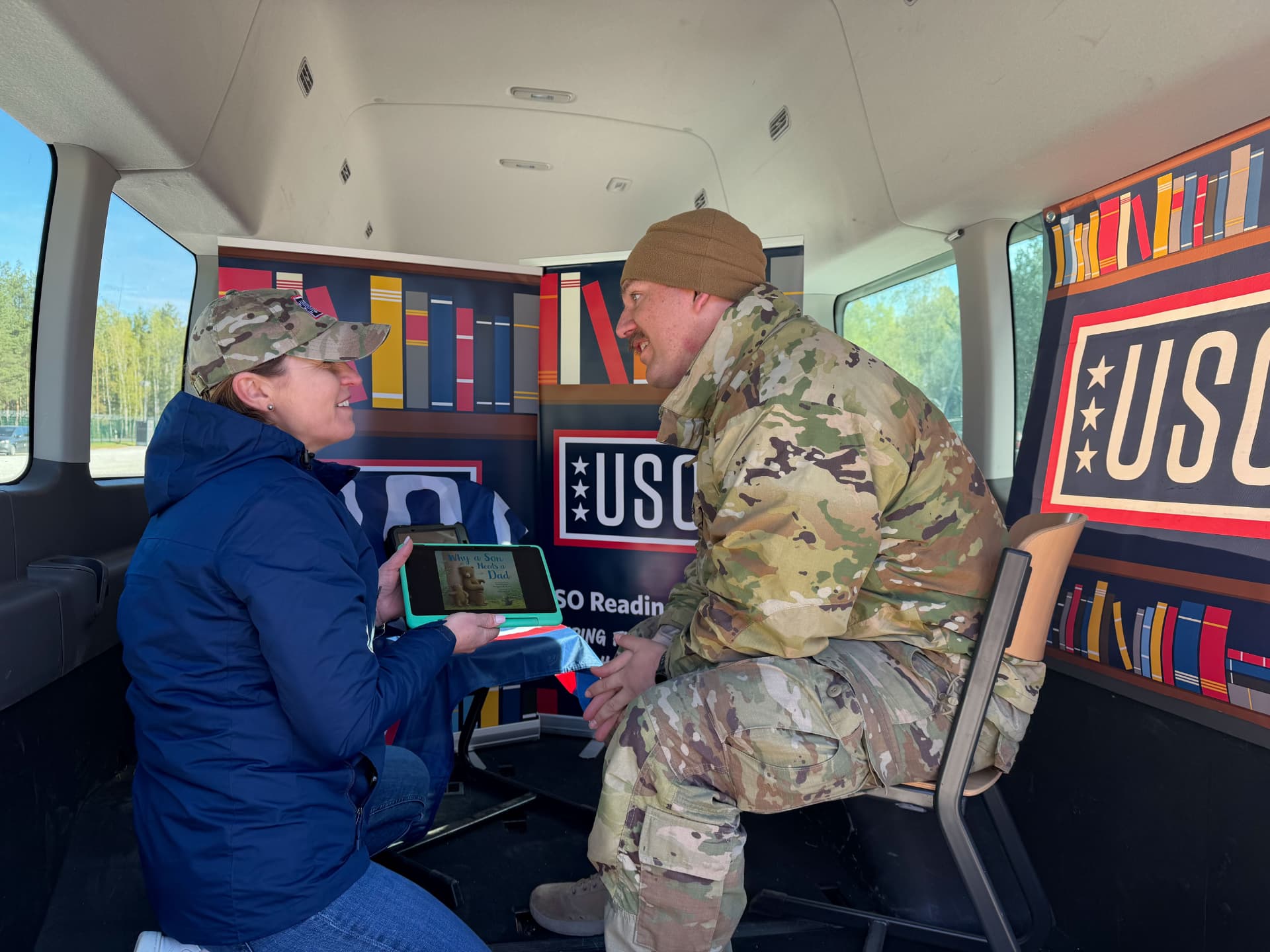 A USO staff member showing a service member the USO Reading Program tablet inside a mobile van.