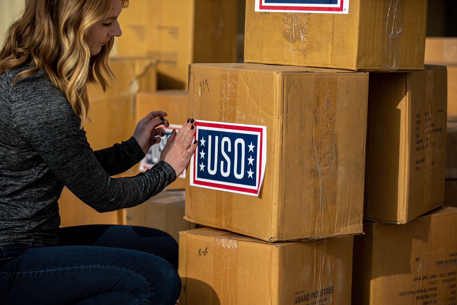 A volunteer placing USO labels on stacked care-package boxes.