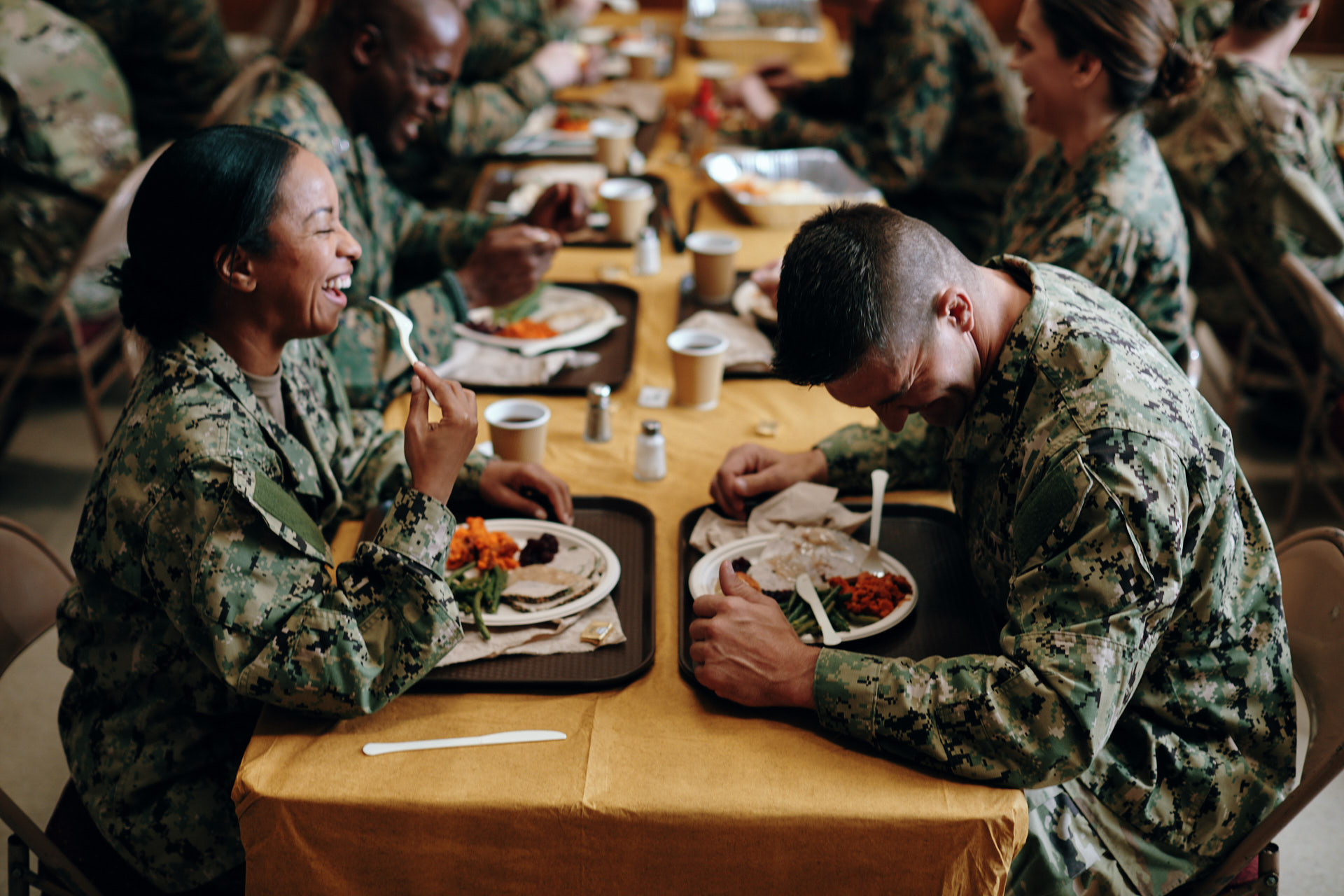 Service members laughing together over a holiday meal at a long table.